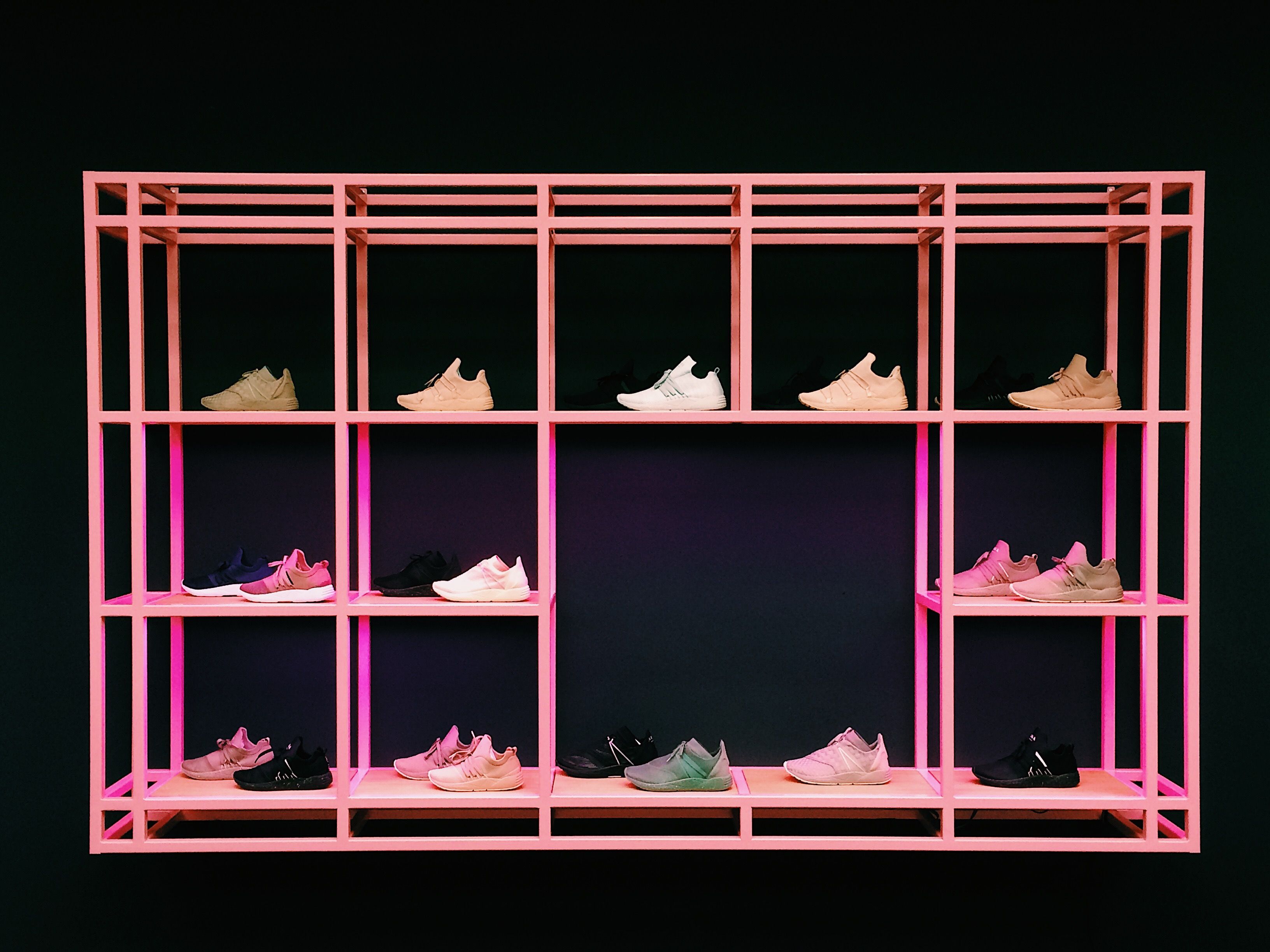 Colorful sneakers arranged on a pink shelf, showcasing a varied new shoe collection.