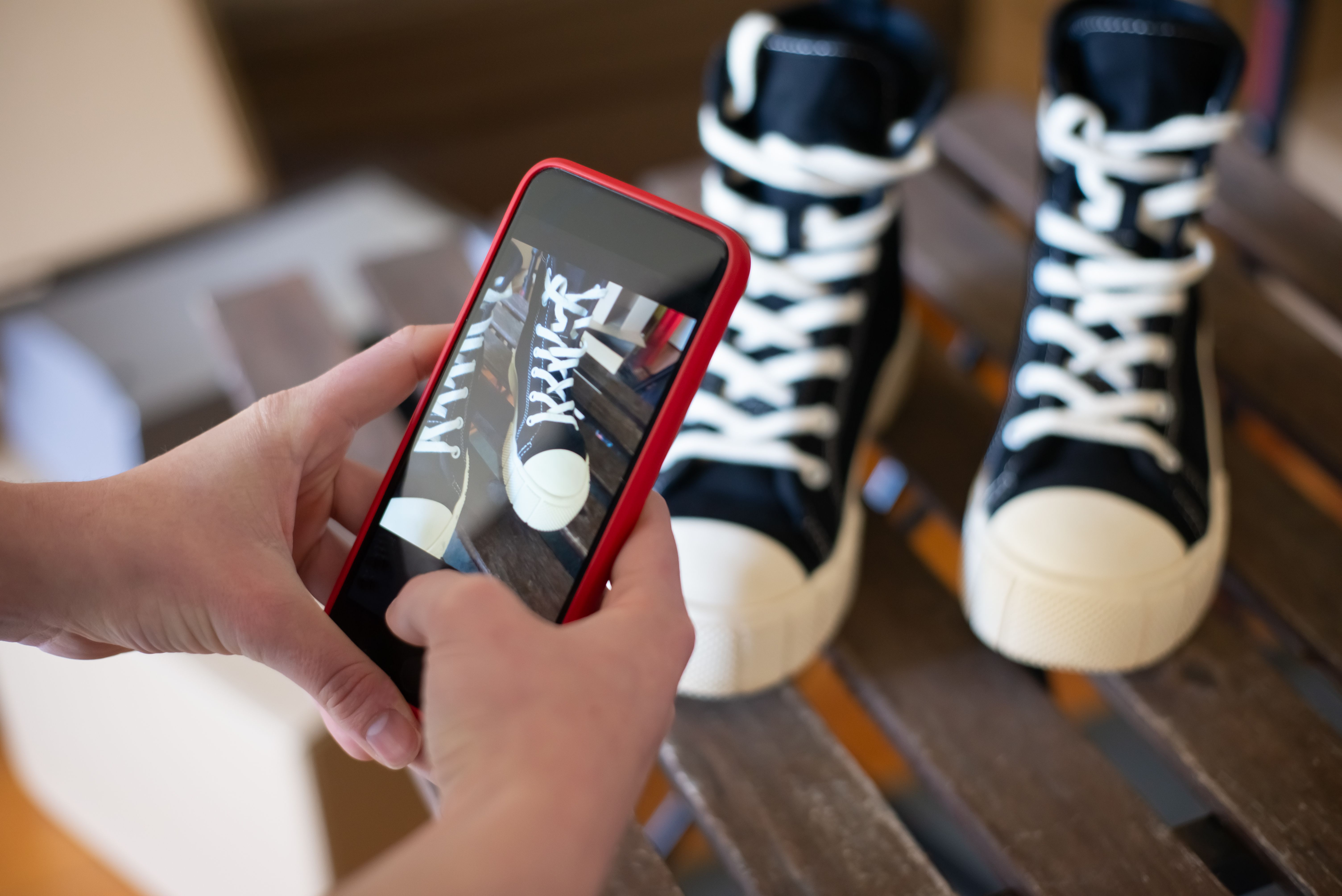 Hands using a smartphone to photograph black sneakers for social media product content.